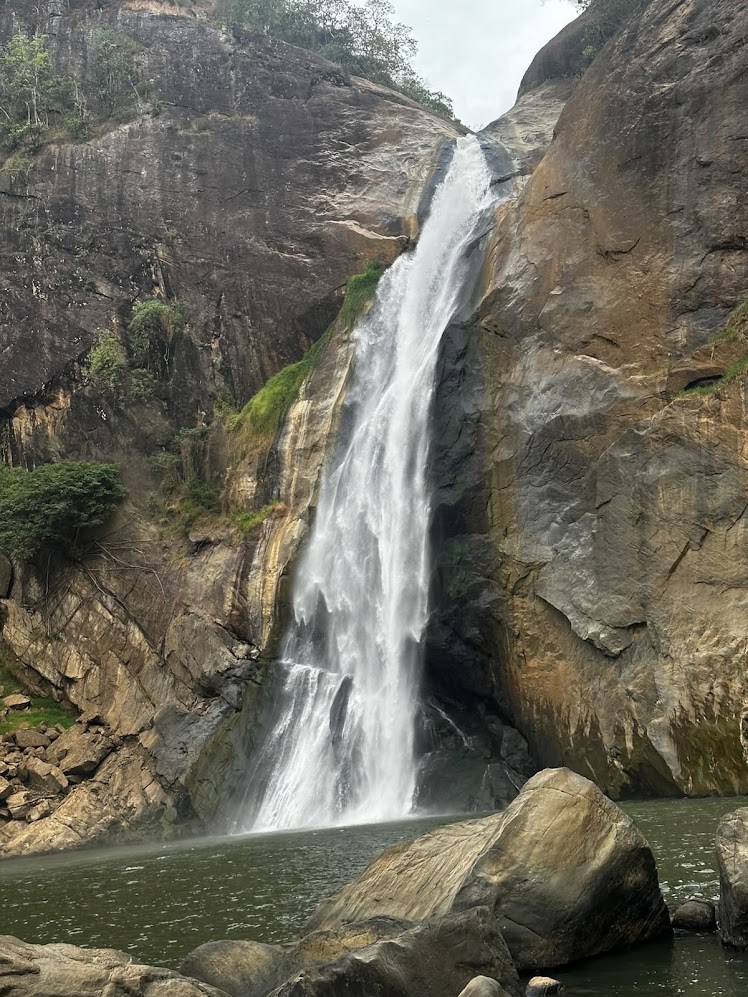 A tall waterfall descending between rock faces into a pool